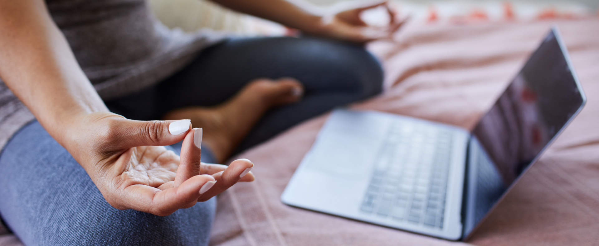 A person sitting in a meditative position while attending an online session on a laptop, symbolizing access to twice-monthly open Zoom sessions with master teachers during yoga teacher training.