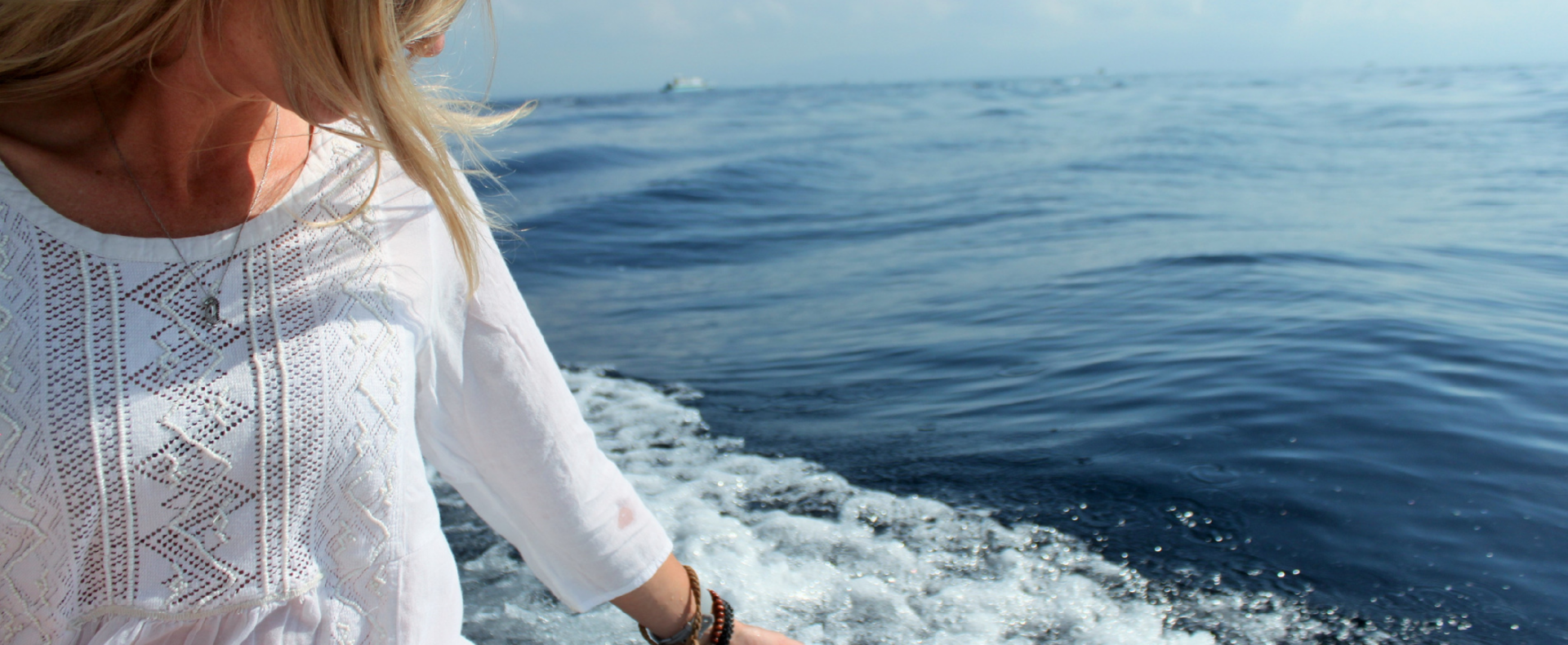 A person wearing a light white top, enjoying a boat ride on the serene waters of Bali. Embrace the tranquility while saving $300 USD with our Bali early bird rate for yoga teacher training.