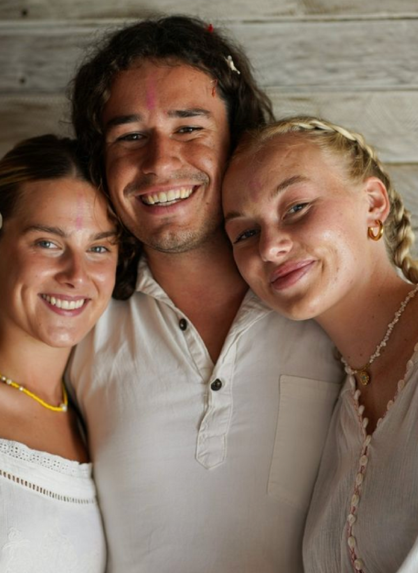 Three smiling individuals embracing each other during a yoga teacher training session, radiating a sense of unity and joy. An opportunity to change your life forever through yoga and community.