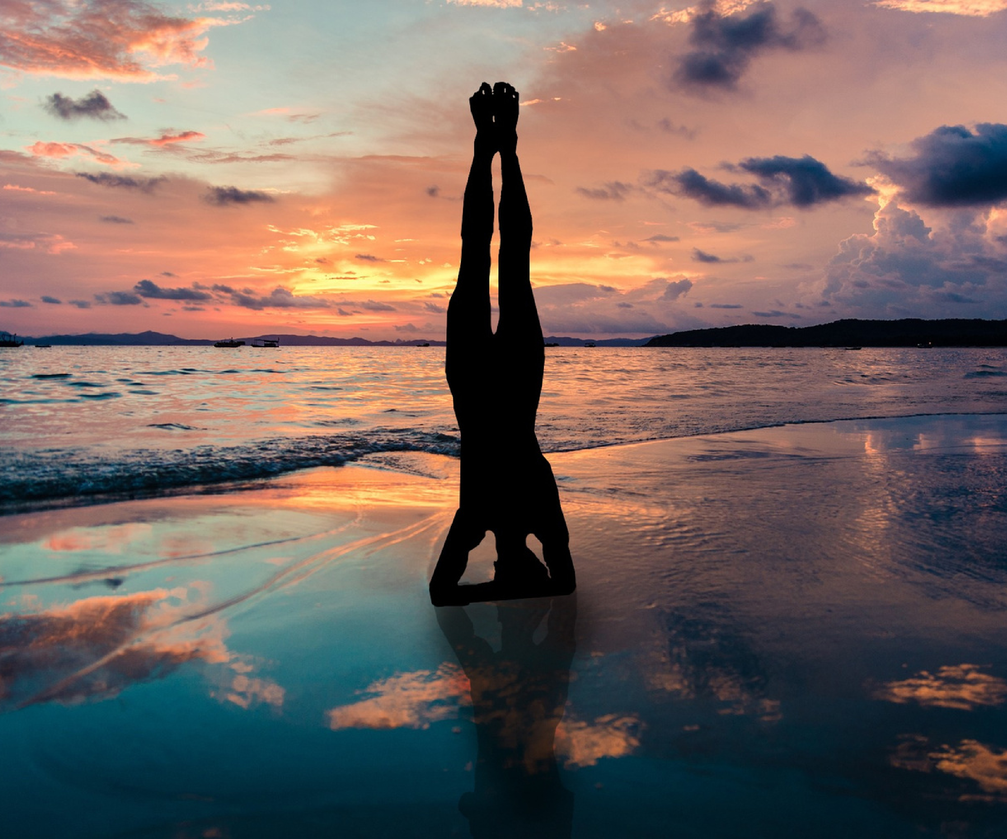 Silhouette of a person in a headstand on the beach at sunset, embodying strength and balance during yoga teacher training. Deepen your own yoga practice in a tranquil, natural setting.