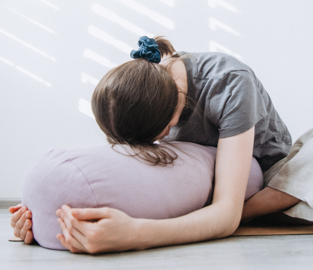 A woman practicing a Yin Yoga pose, resting forward on a lavender bolster in a peaceful, light-filled space, embodying relaxation and mindfulness.
