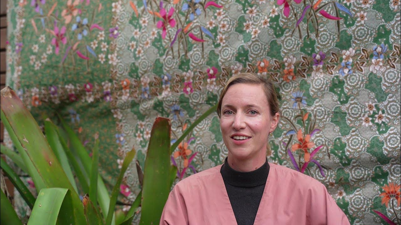 Kristen smiling in front of a colourful floral fabric backdrop during a video interview