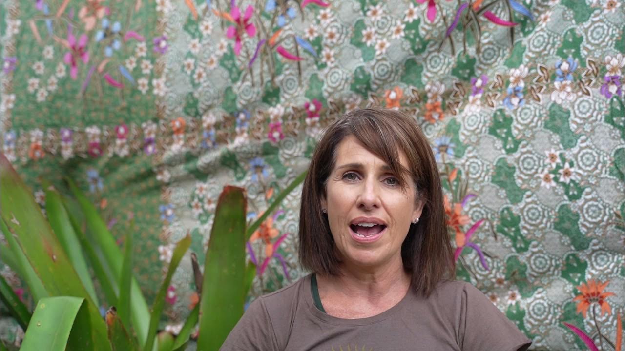 Margaret sharing her experience in front of a colourful floral backdrop with tropical plants