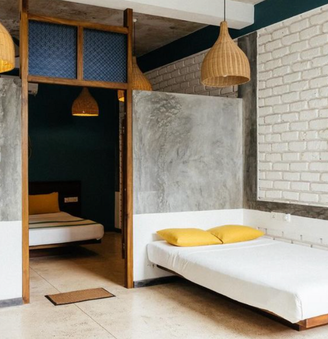 Modern minimalist Sri Lanka yoga retreat accommodation with industrial-style decor, concrete finishes, and simple white beds with yellow pillows.