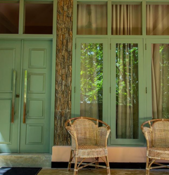 Front view of a serene Sri Lanka yoga retreat entrance with mint green doors, tall windows, and rustic wicker chairs.