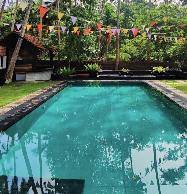 Outdoor swimming pool surrounded by lush tropical gardens with colourful flags overhead at a Sri Lanka yoga retreat.