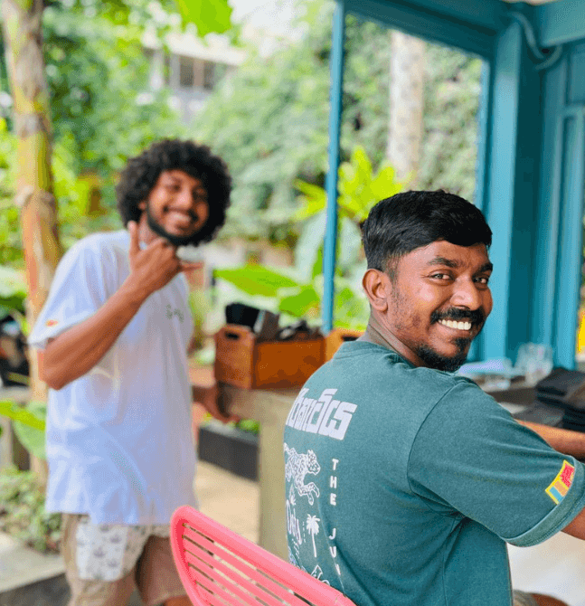 Two smiling local staff members at a Sri Lanka yoga retreat, standing in a lush tropical setting.