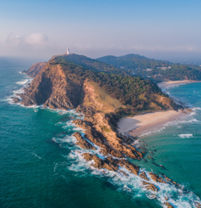 Aerial view of Cape Byron in Byron Bay with the iconic lighthouse on the cliff and turquoise ocean waves below.