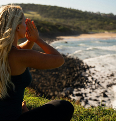 Woman meditating on a cliffside overlooking the ocean in Byron Bay, practising mindfulness during yoga teacher training.