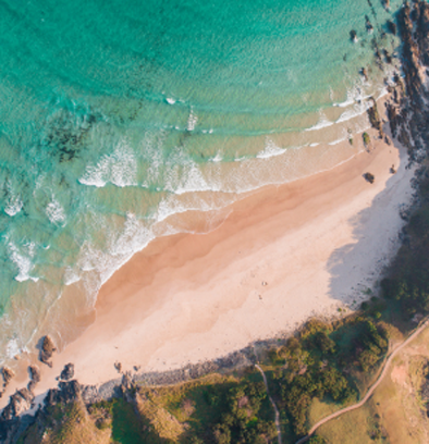 Aerial view of turquoise waves and sandy beach with lush greenery at Byron Bay, Australia.