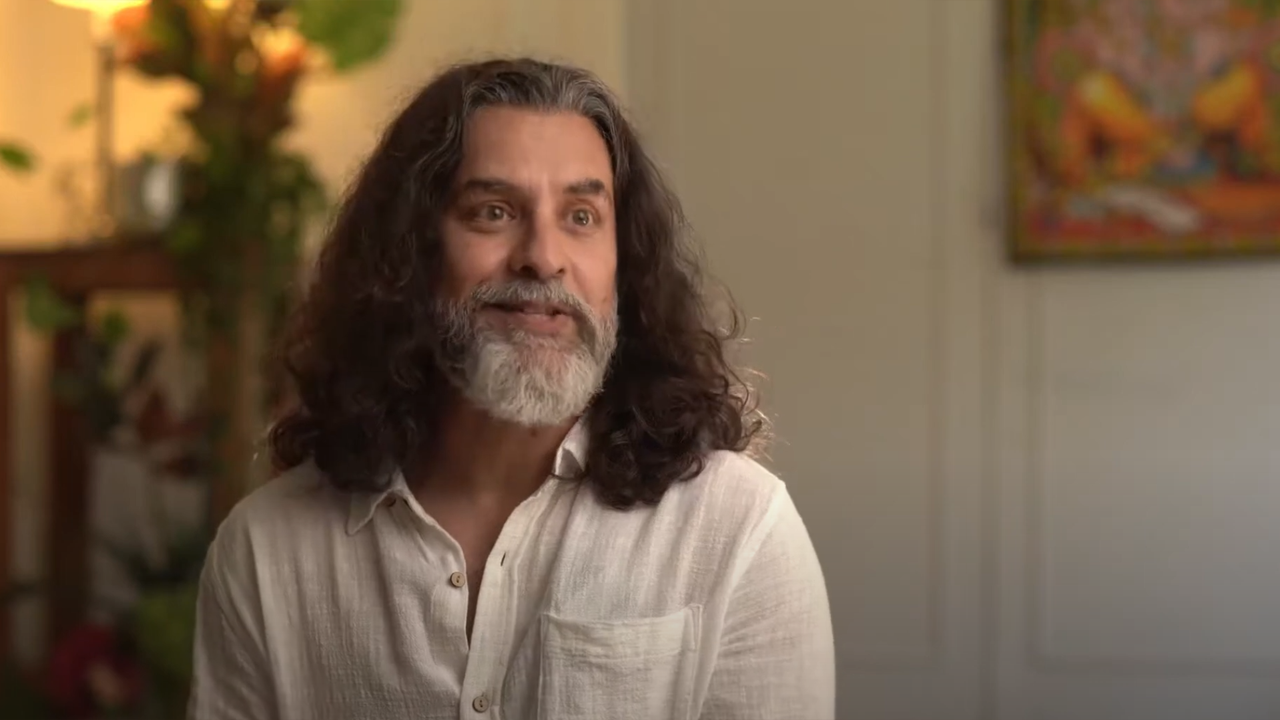 Smiling man with long curly hair and beard sharing his yoga journey during an interview.